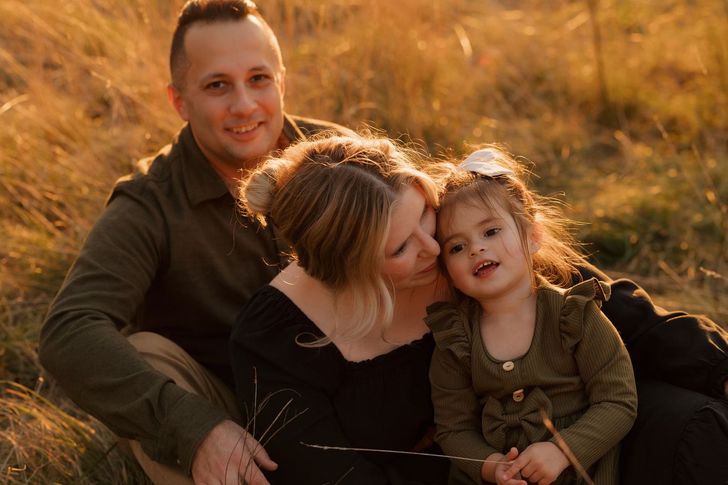 A family laughs together while sitting in tall grass during golden hour.