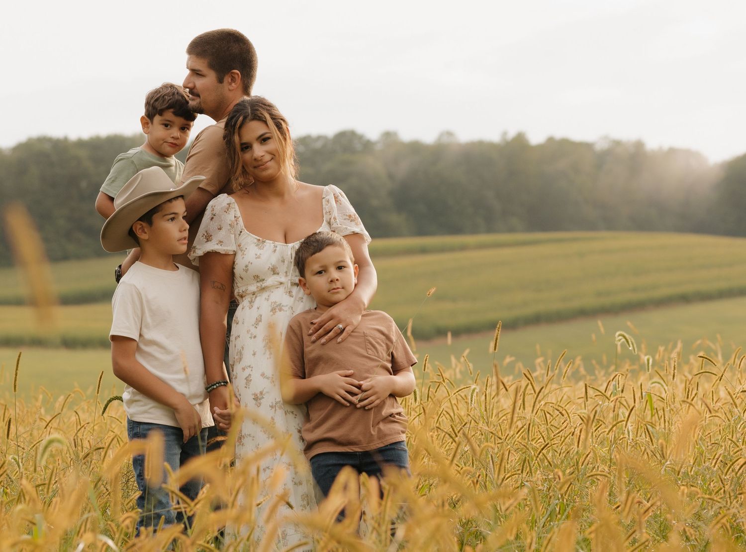 Family enjoying tender moments together in a golden wheat field at sunset.