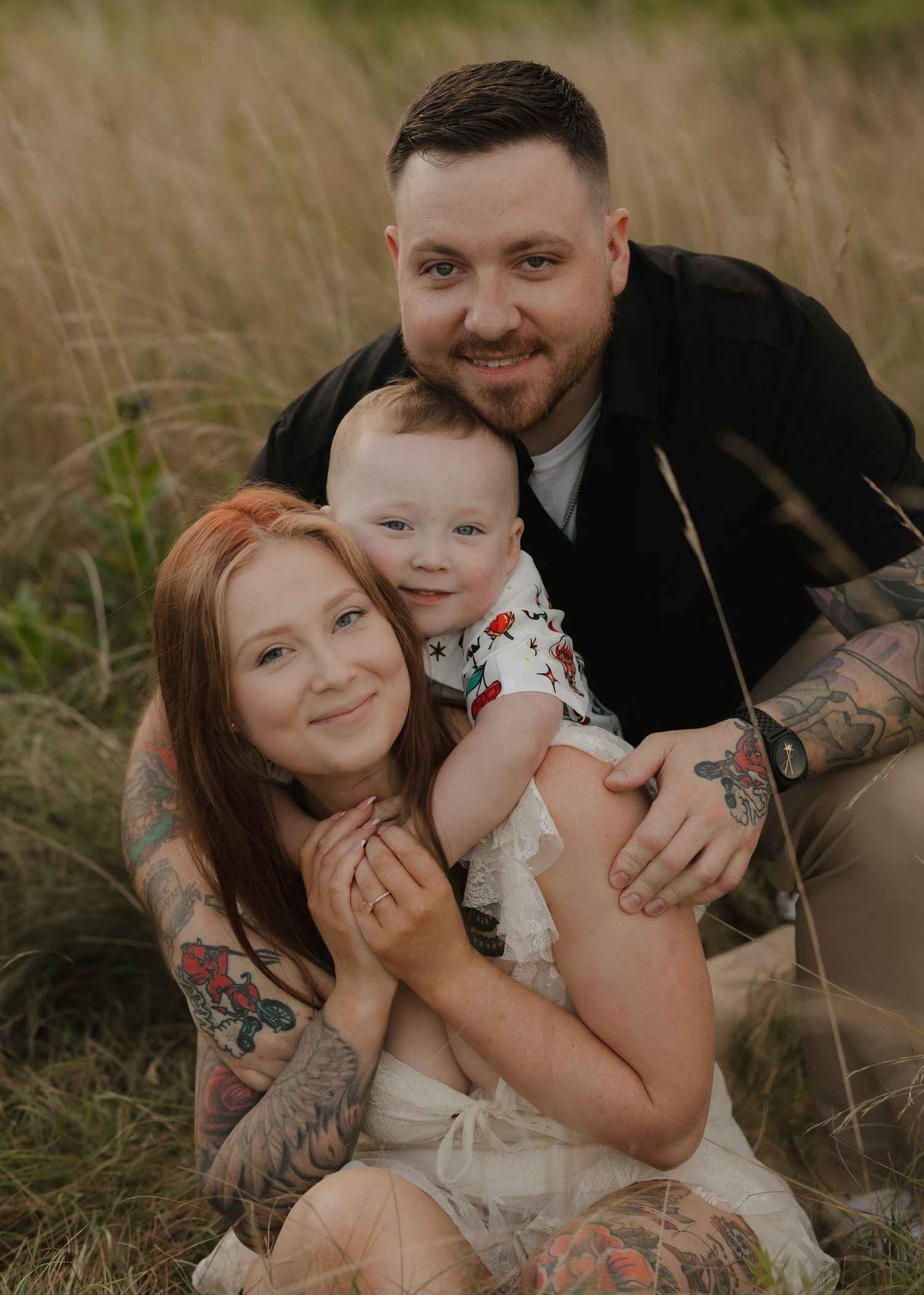 Family of three snuggling close together for intimate outdoor portrait in grassy field.