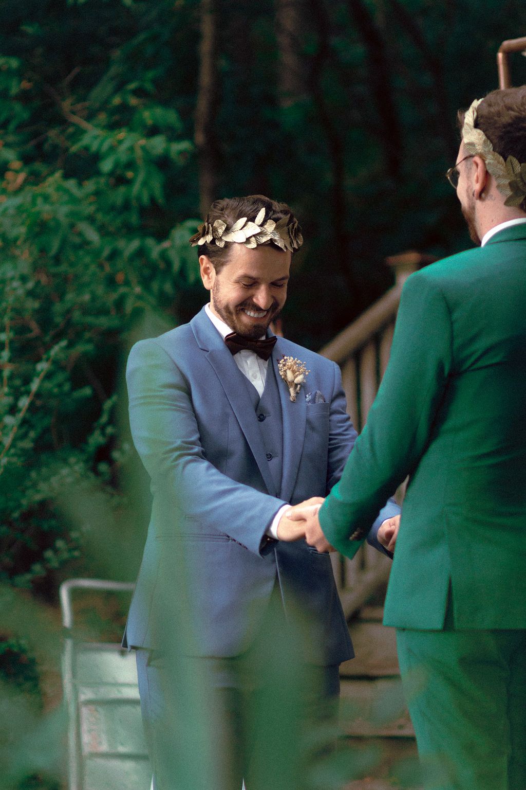 Same-sex couple in dark blue and green wedding attire surrounded by lush greenery at Fantasy Farm Toronto
