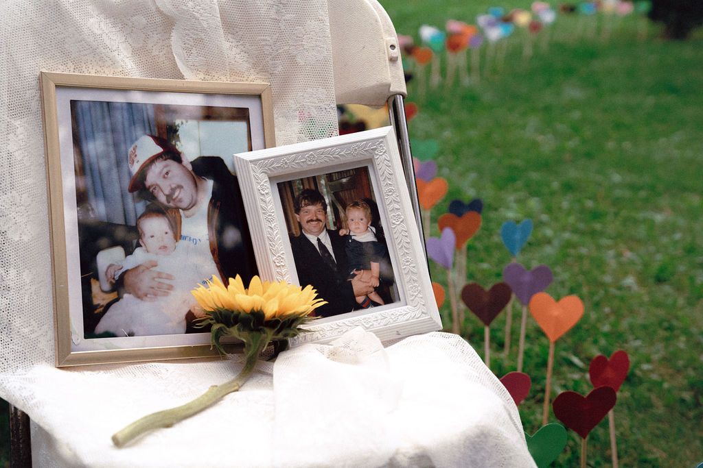 Memorial chair draped in white fabric with framed photos of fathers and sunflower at gay wedding Fantasy Farm Toronto