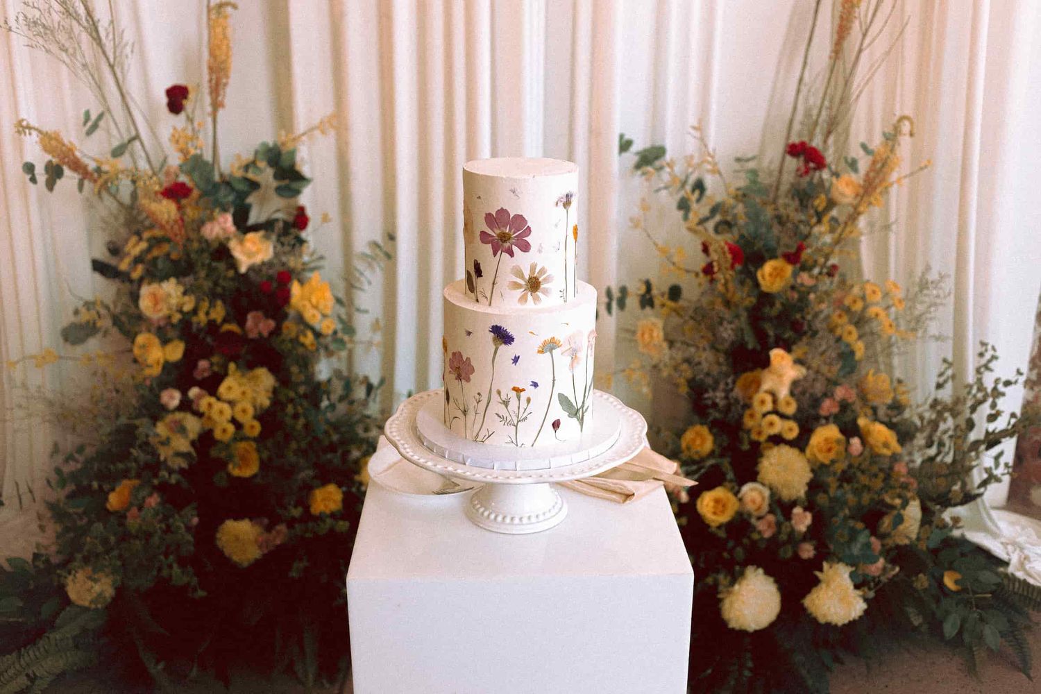 Wedding cake displayed among floral arrangements before the reception.
