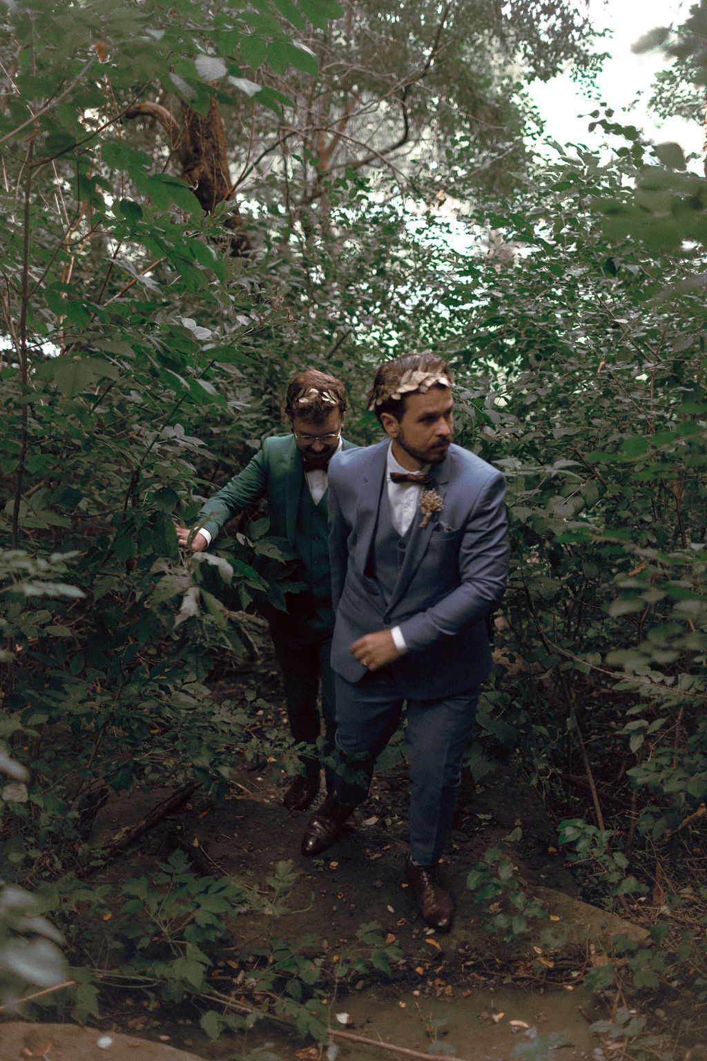 Same-sex couple in dark blue and green wedding attire surrounded by lush greenery at Fantasy Farm Toronto