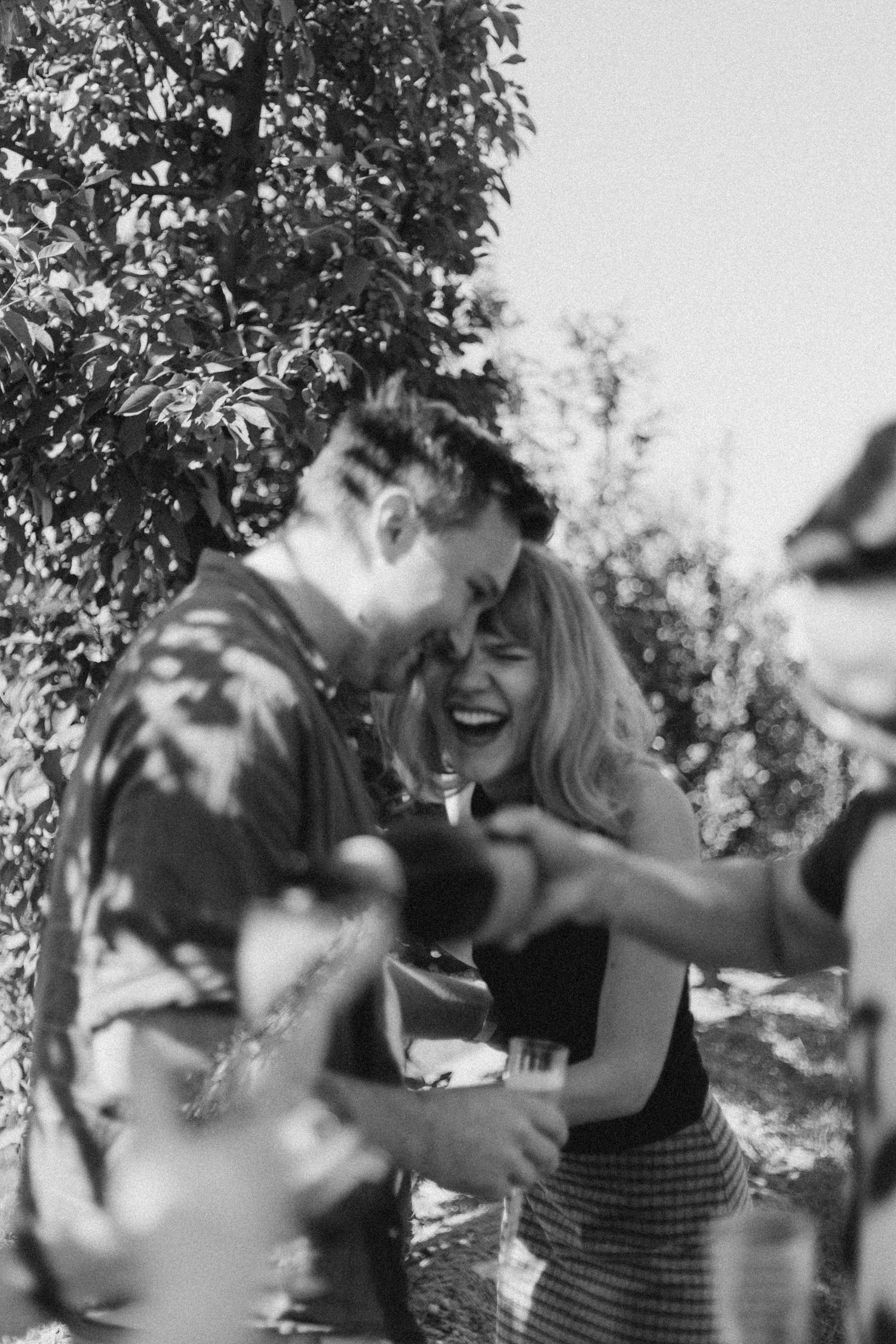 Surprise engagement at Chudleighs Apple Farm, couple laughing together as guests serve champagne in the background