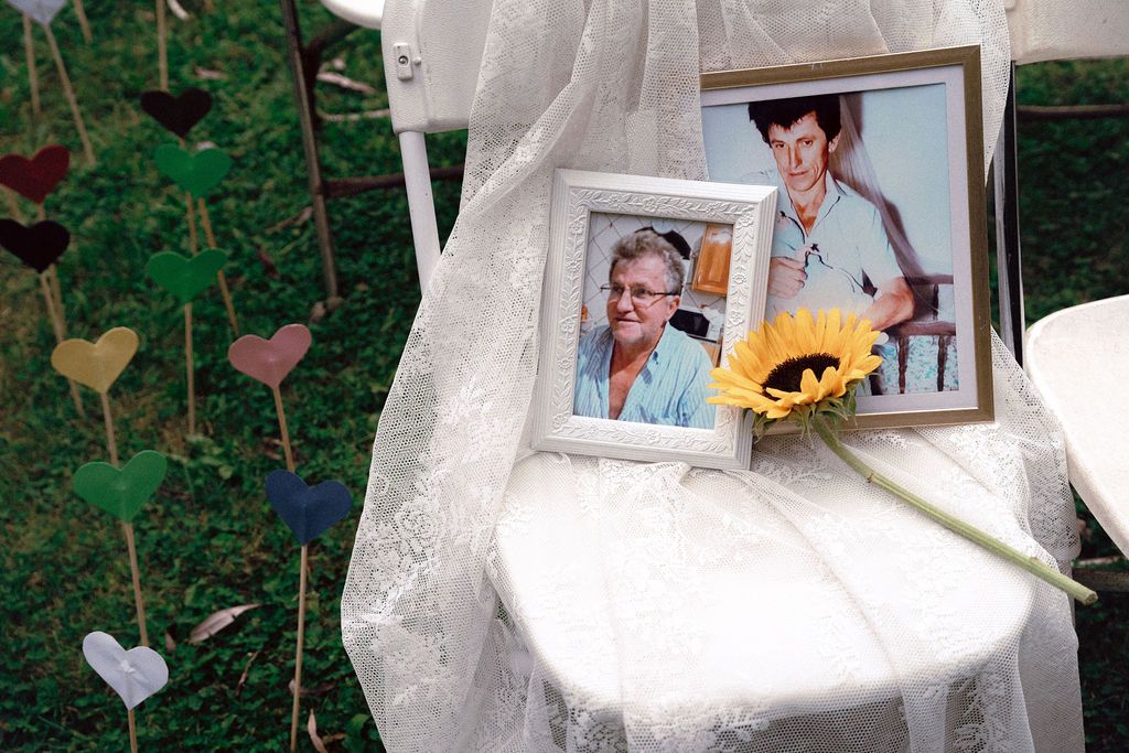 Memorial chair draped in white fabric with framed photos of fathers and sunflower at gay wedding Fantasy Farm Toronto