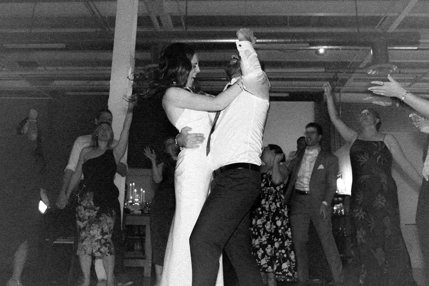 Newlyweds and guests dancing together during a lively wedding reception.