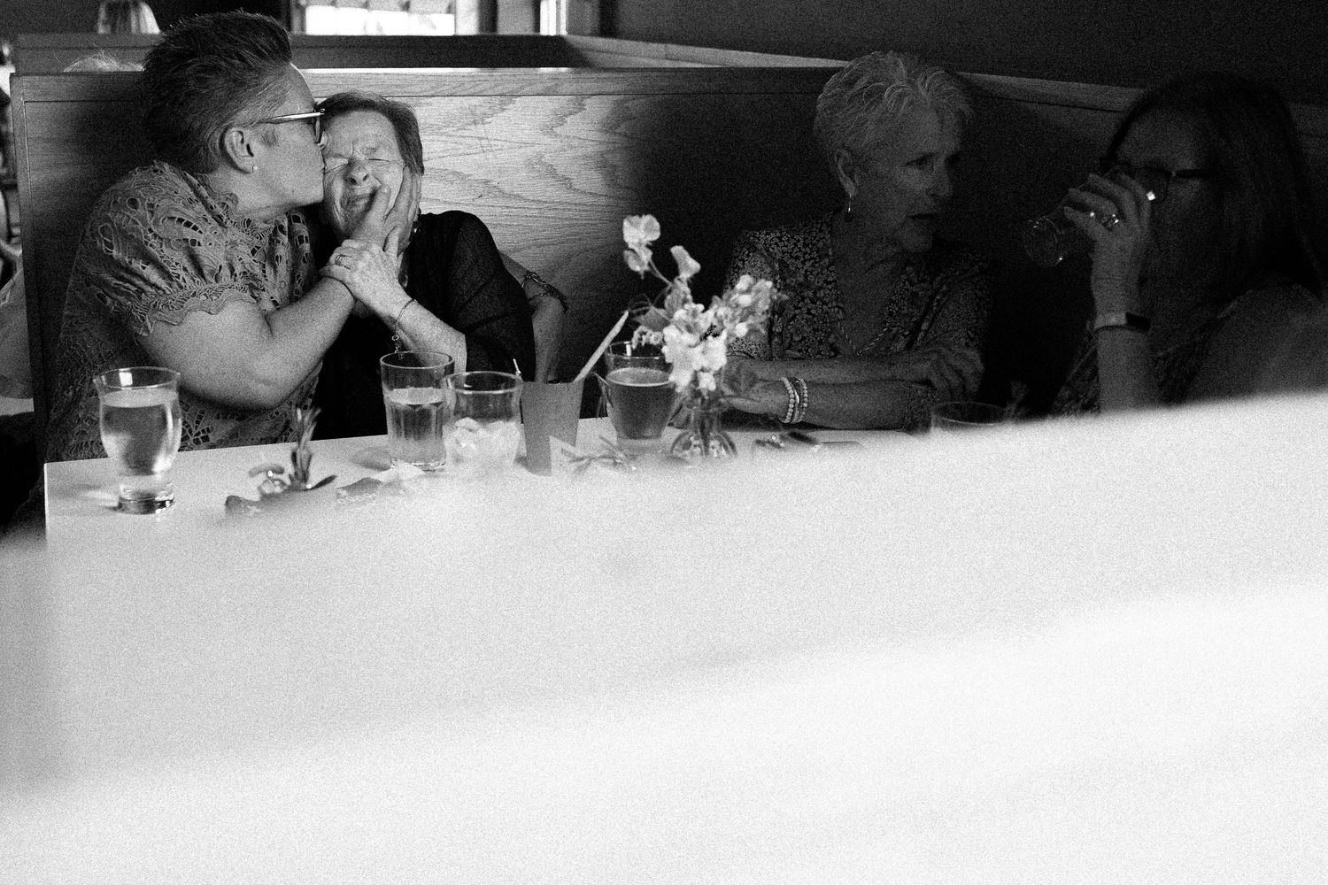 Candid wedding moment in Toronto capturing the mother of the bride kissing her aunt as guests talk beside them, unposed and intimate