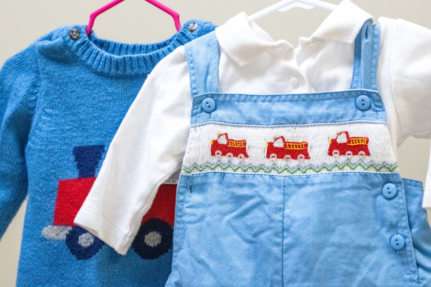 Blue baby boy outfit set with train sweater and smocked fire truck corduroy overalls on a hanger.