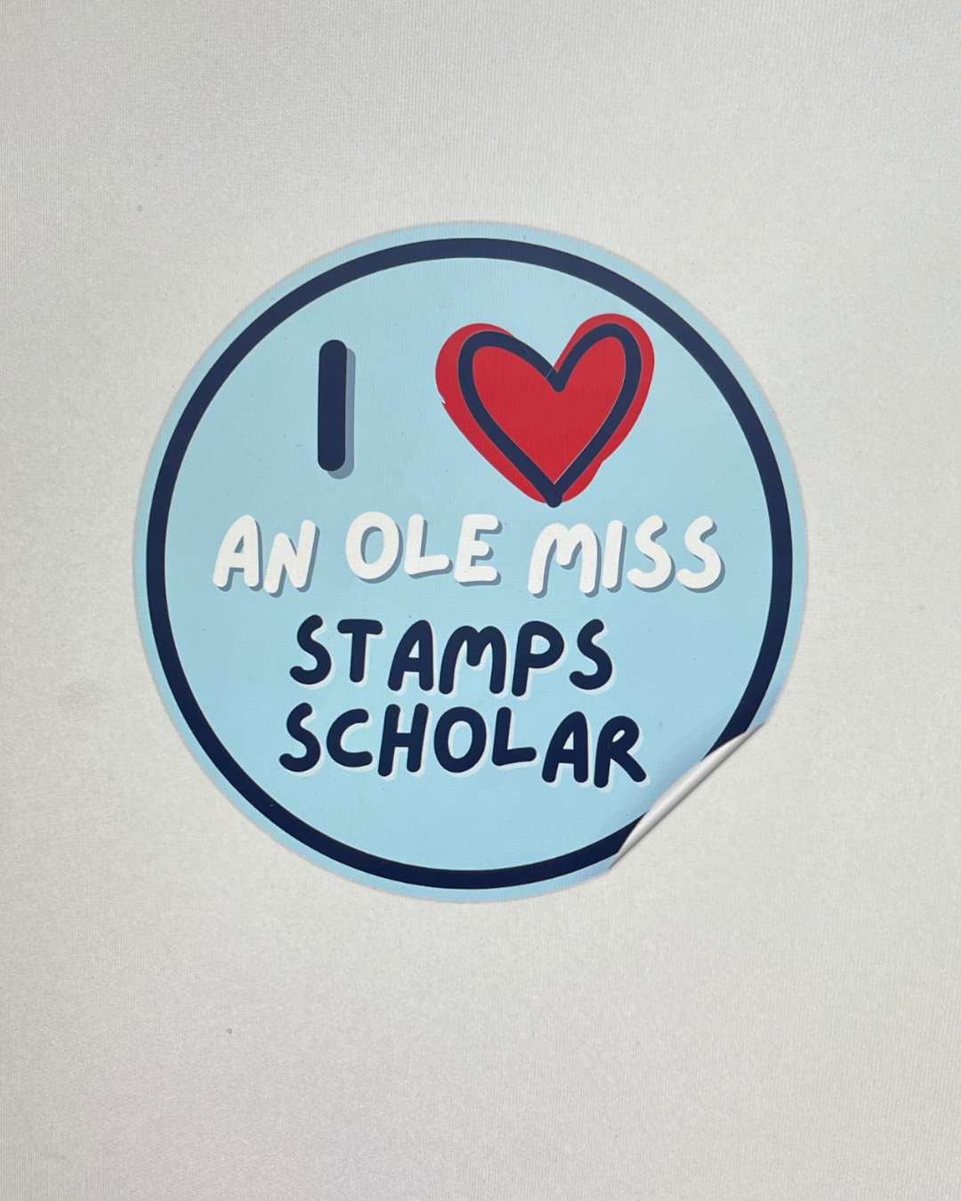 Light blue circular sticker reading I Love An Ole Miss Stamps Scholar with a red heart design.