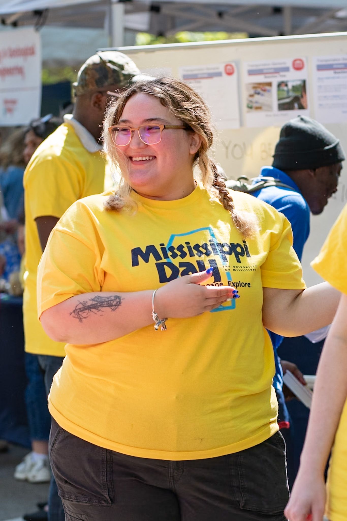 Smiling woman wearing yellow Mississippi Day t-shirt with braided hair at outdoor university event.