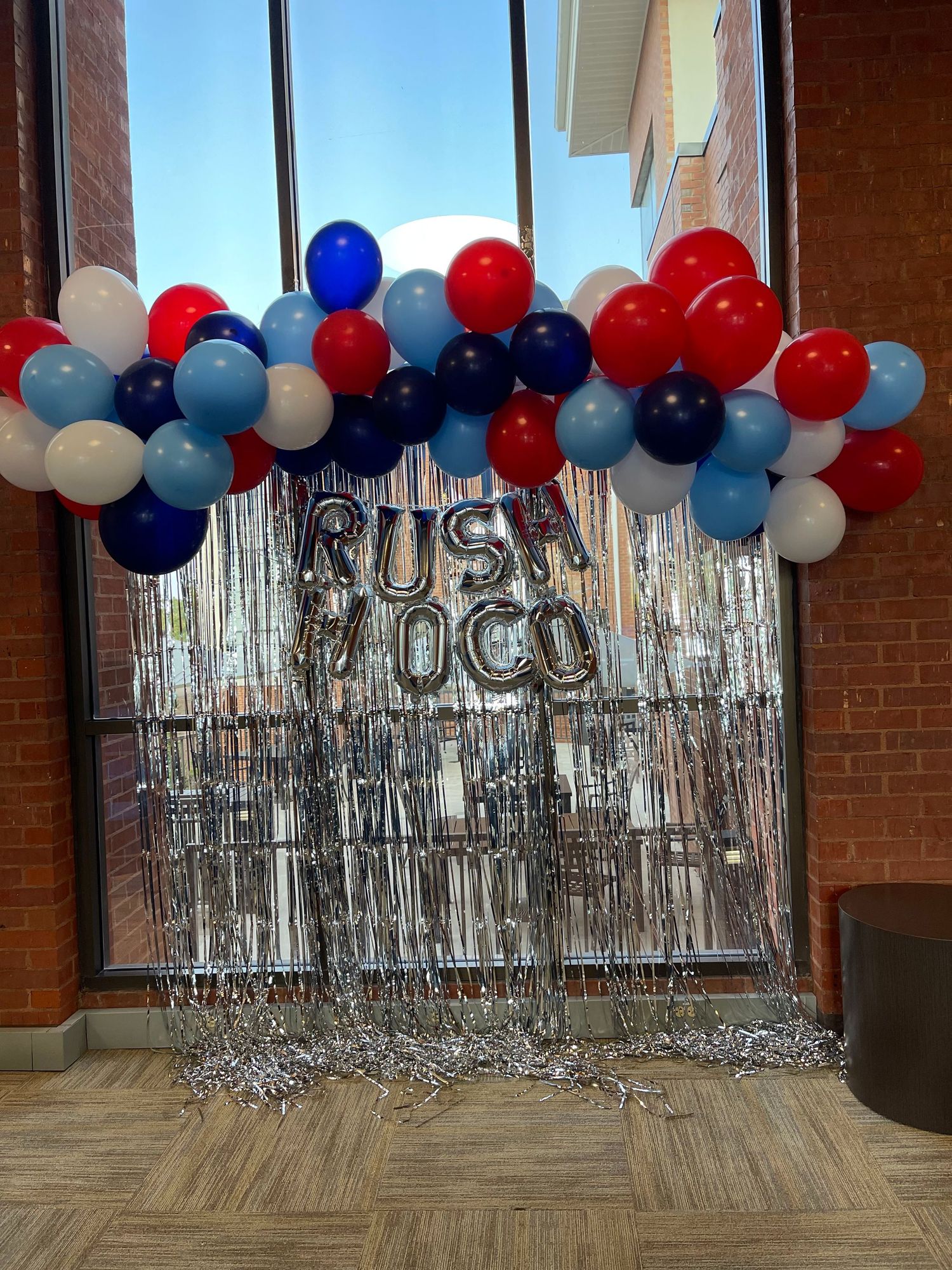 Red, white, and blue balloon garland with silver tinsel backdrop and RUSH OCO mylar letter balloons for a festive event.