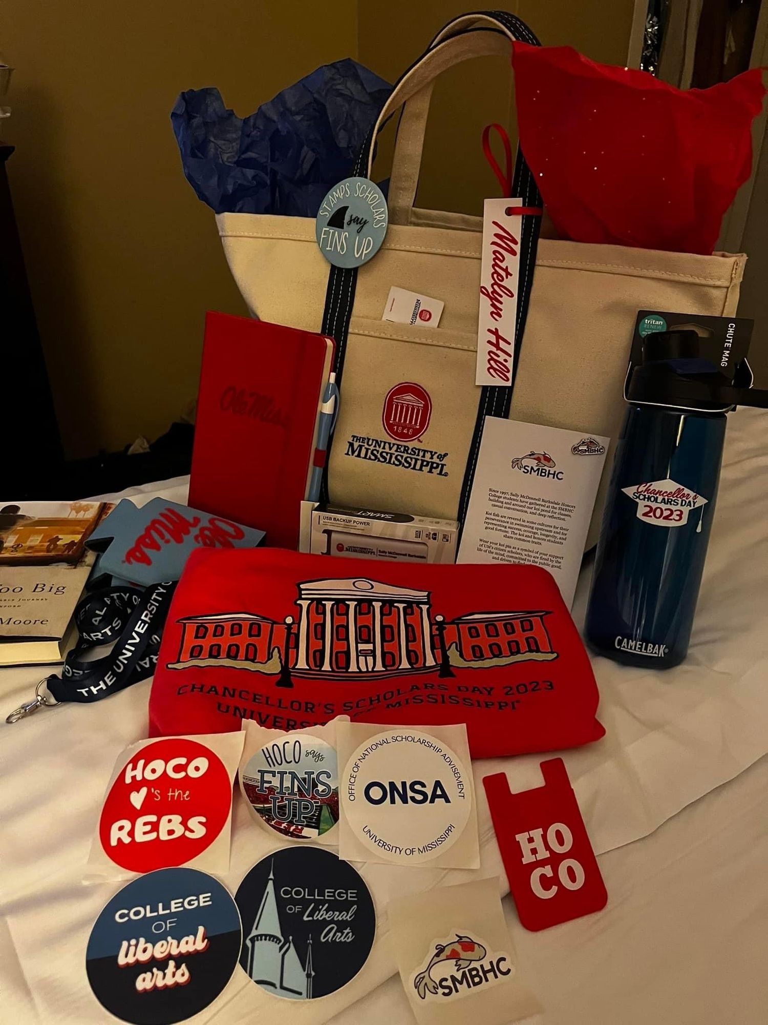 University of Mississippi Chancellor's Welcome 2023 gift bag with HOCO, ONSA, Liberal Arts stickers, tote, and water bottle.