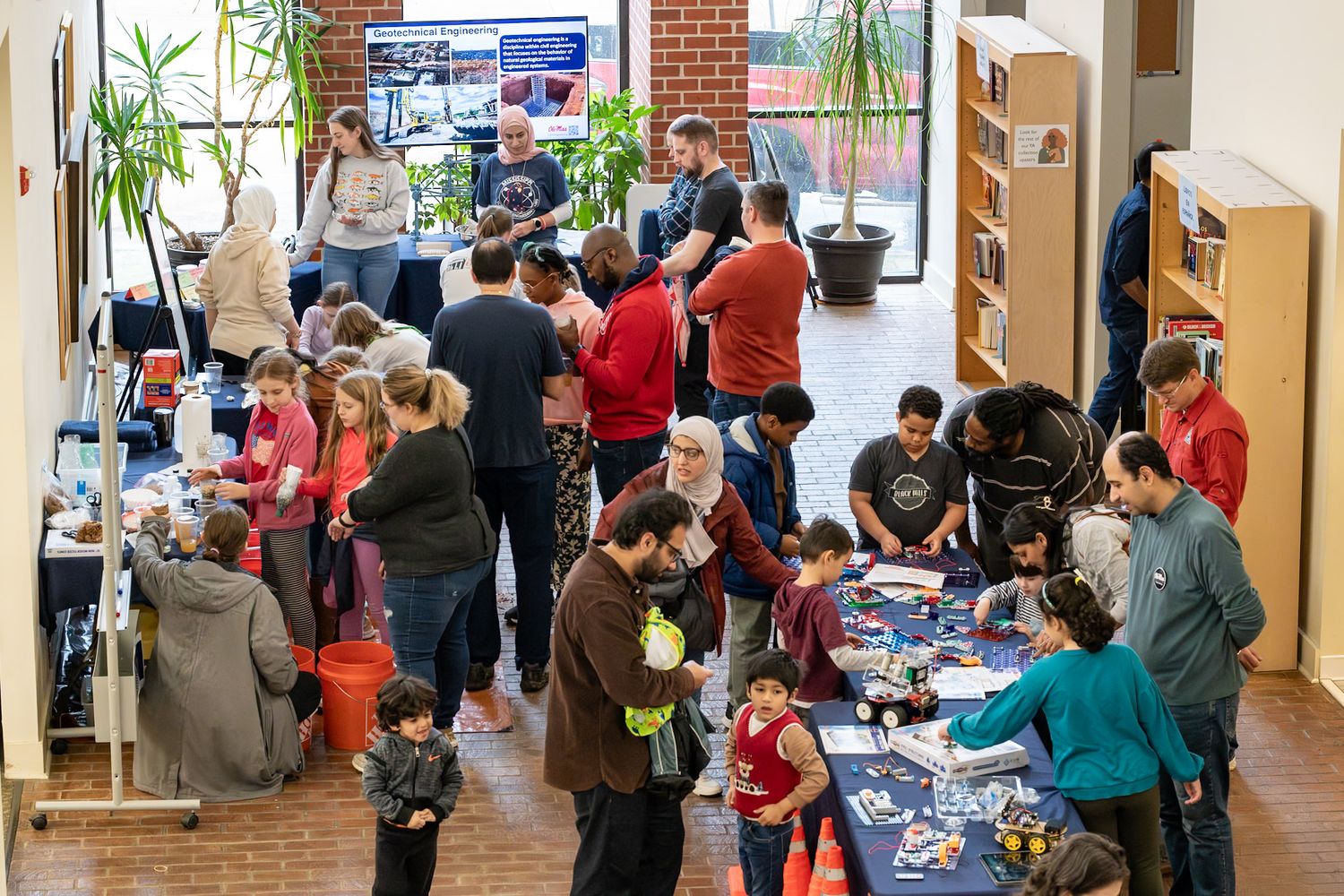 Busy indoor science fair event with families and children exploring educational activity tables in a bright community space.