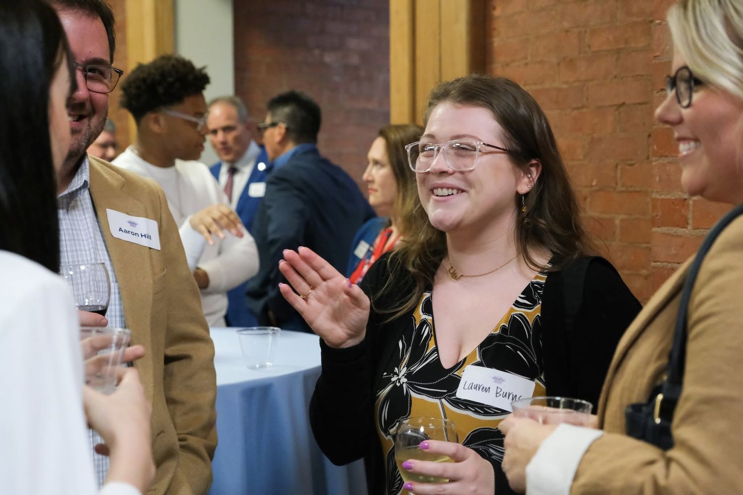 Professionals networking at a formal event, smiling and conversing while holding drinks in a bright venue.