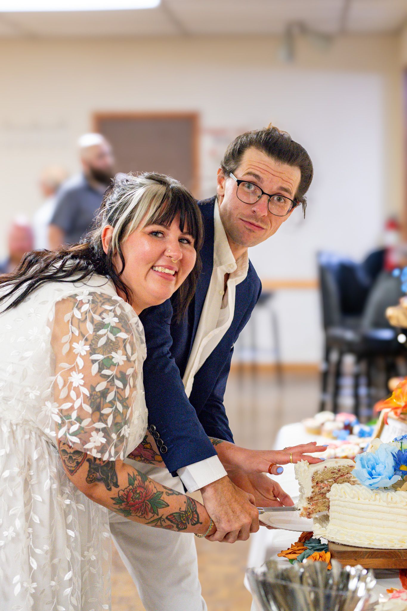 A couple cutting their wedding cake together at a reception while smiling at the camera.