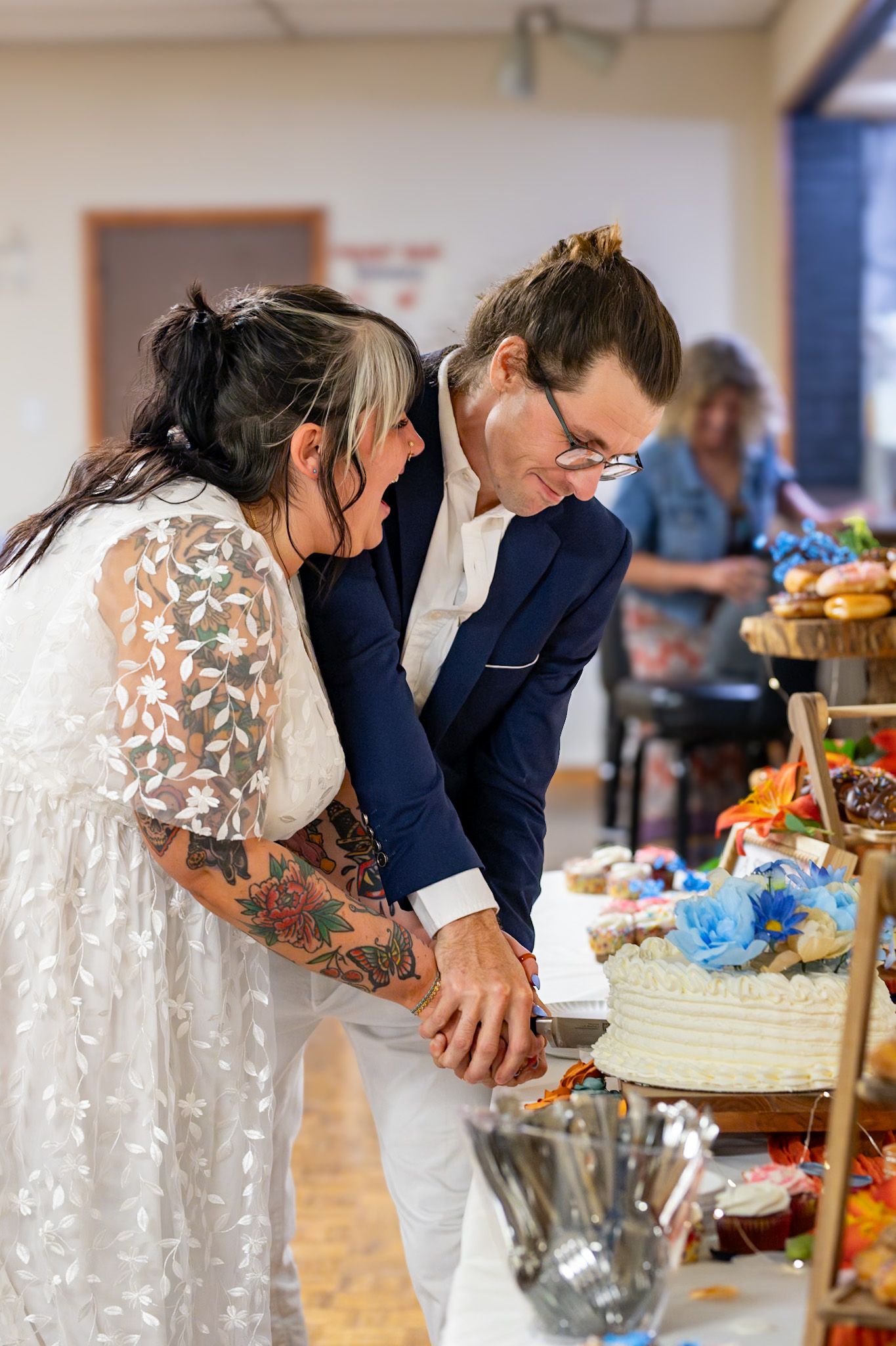 Wedding couple shares an intimate moment while cutting their white frosted cake together at a reception.