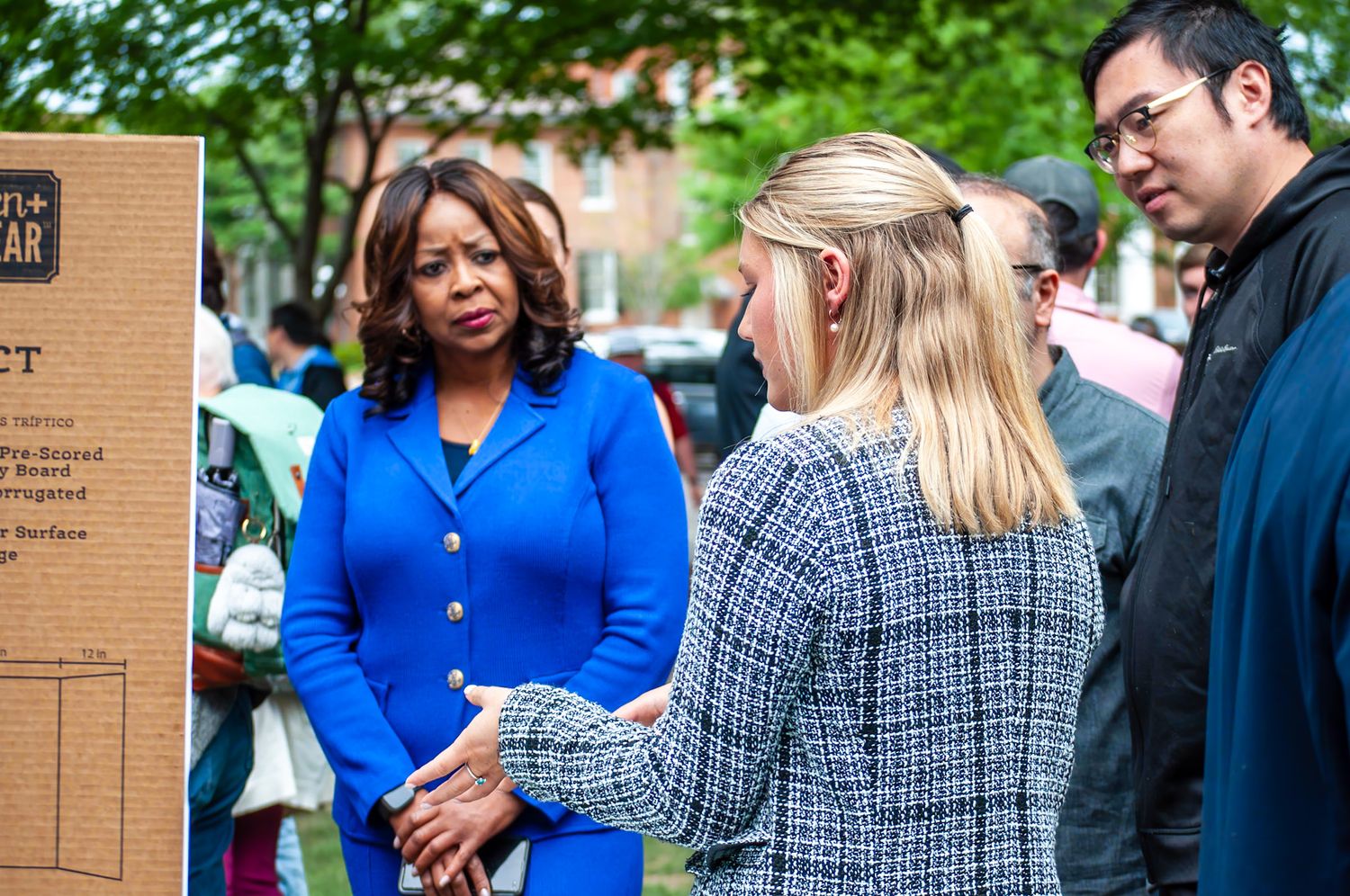 Professional women in business attire engage in outdoor conversation at a formal event, with a man standing nearby.
