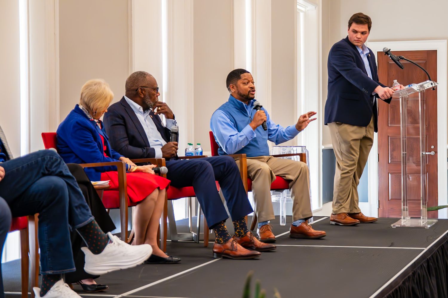 Panel discussion with four speakers seated on stage, one man speaking into microphone at a professional conference event.