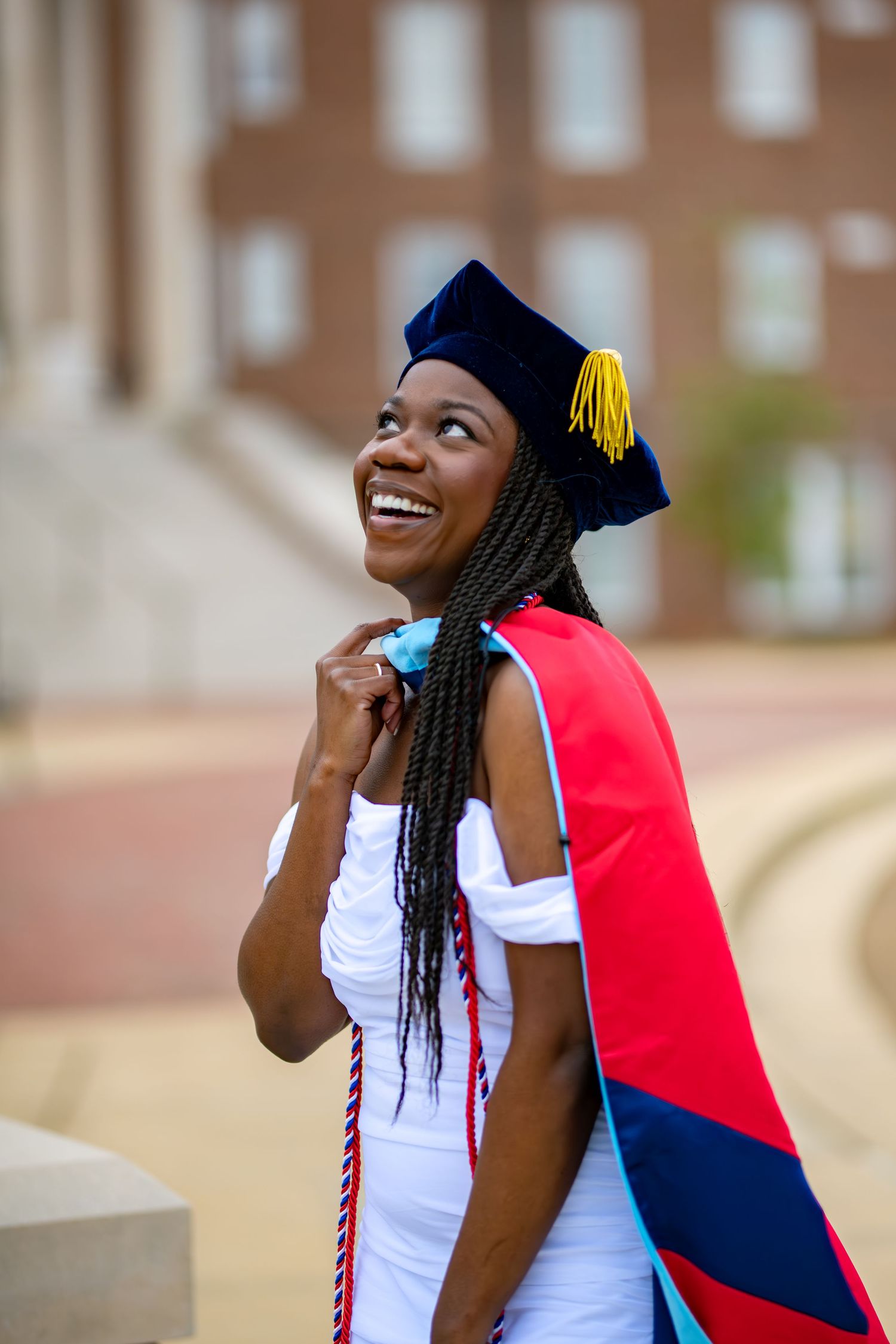 Graduate in academic regalia with colorful stole and tassel cap on campus grounds.
