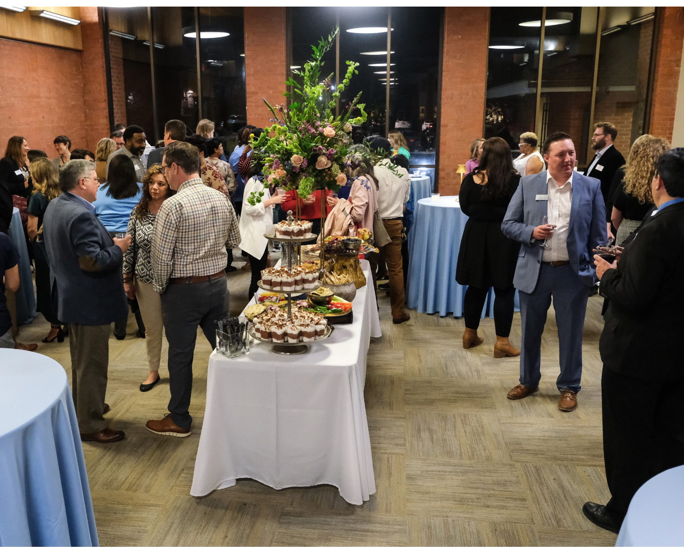 Guests mingle at an elegant university reception with floral centerpiece and catered food display.