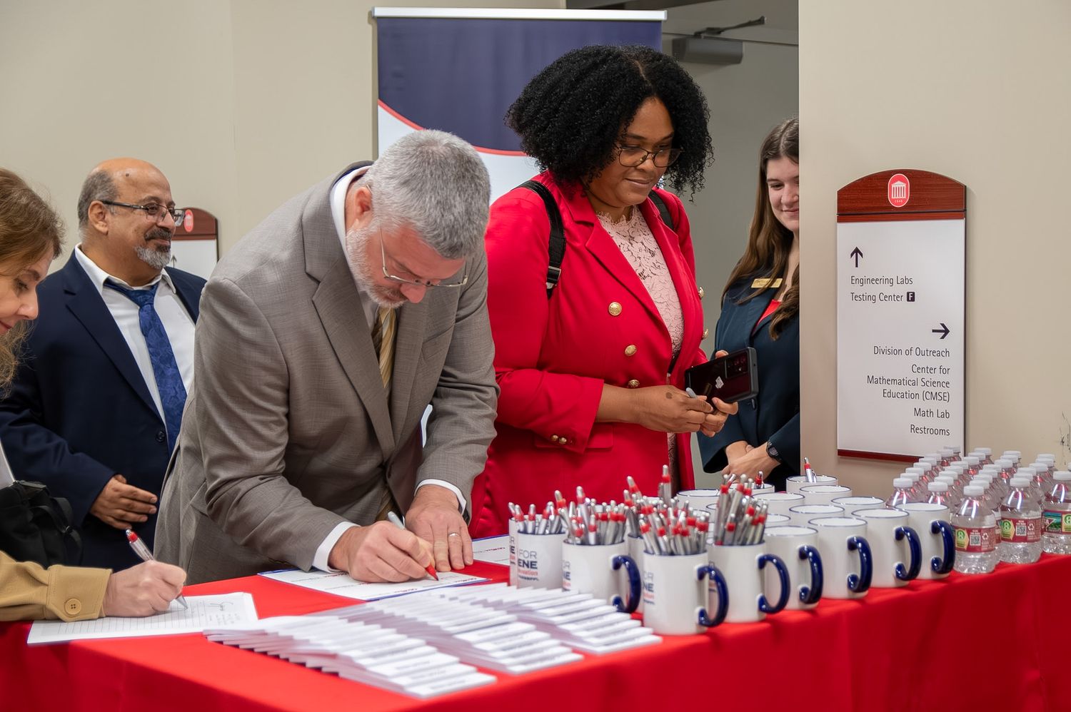 Officials signing documents at a formal ceremony table with red notebooks and decorative items displayed.