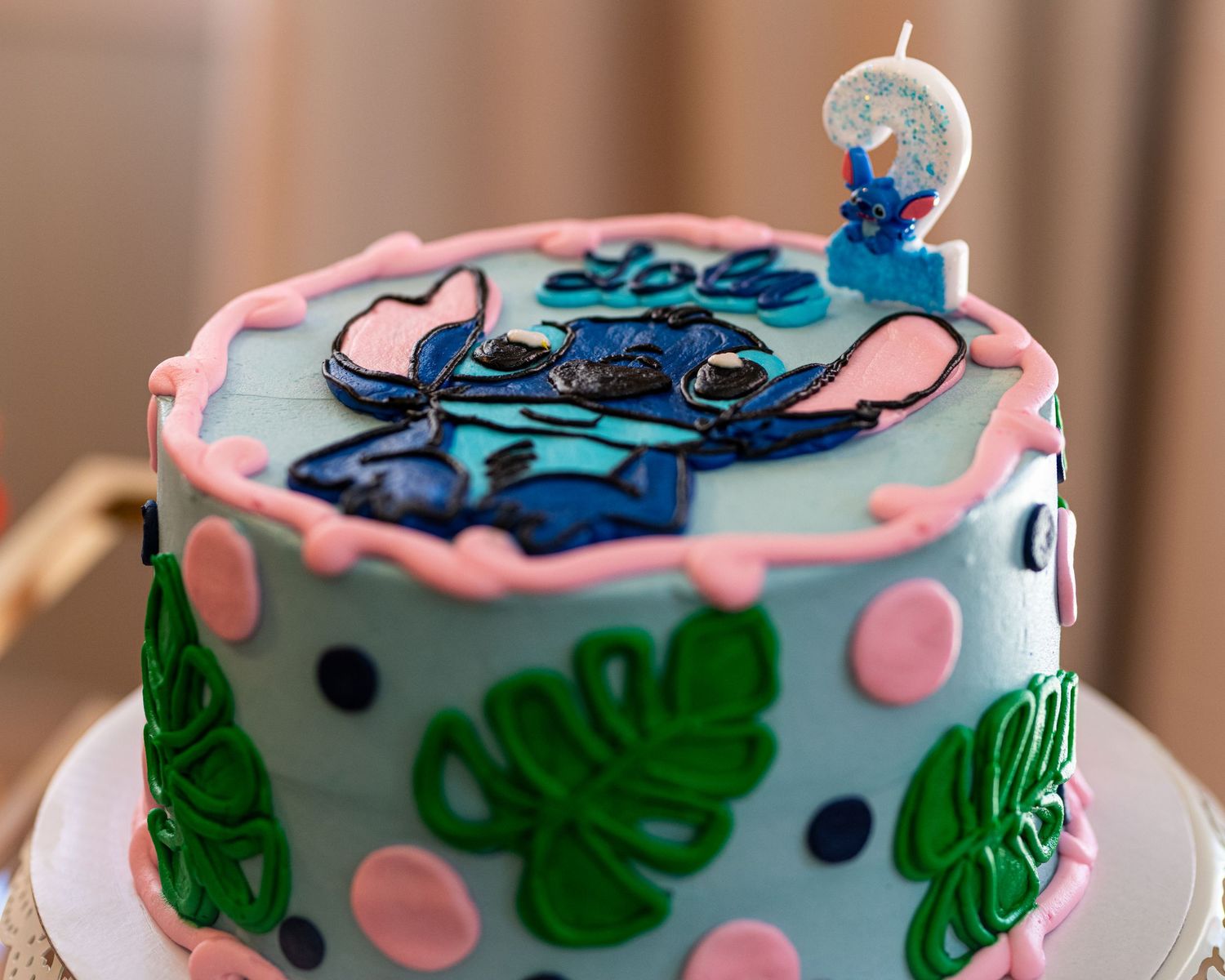 A tropical-themed birthday cake decorated with blue butterflies, pink polka dots, green palm leaves, and a number candle on top.