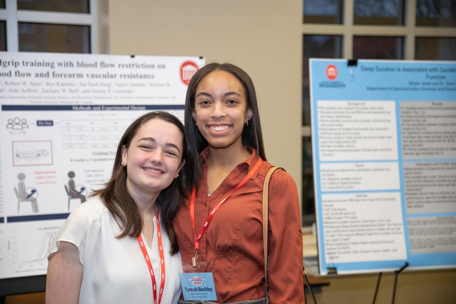 Two young women posing together in front of research posters at an academic conference.