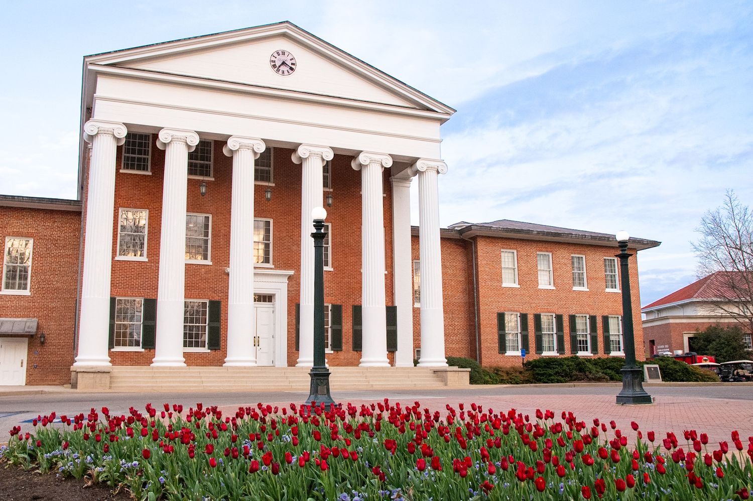 Historic brick university building with white columns and red tulips blooming in foreground under a clear sky.
