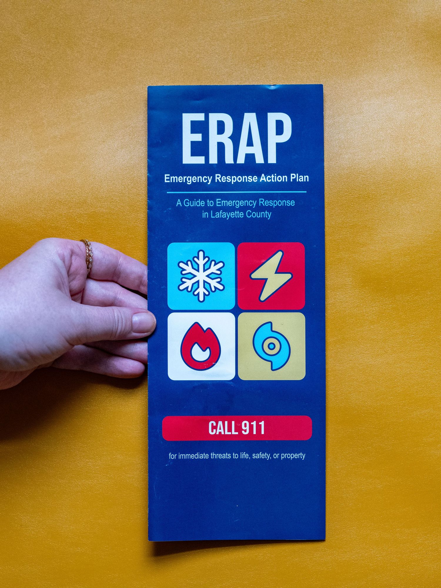 Hand holding ERAP Emergency Response Action Plan brochure for Lafayette County with Call 911 emergency guide.