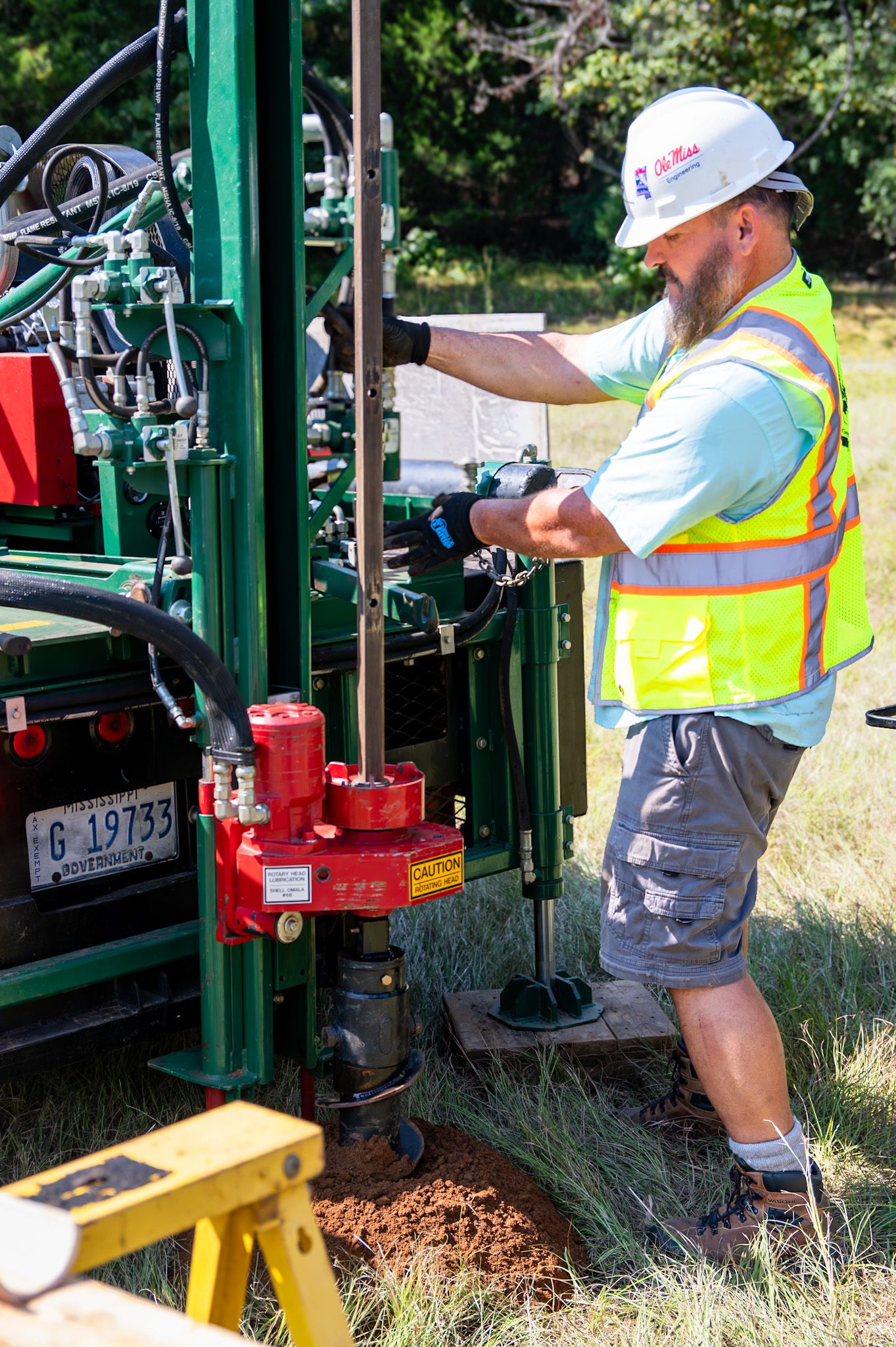 Worker in safety vest and hard hat operating a drilling machine on a construction site outdoors.