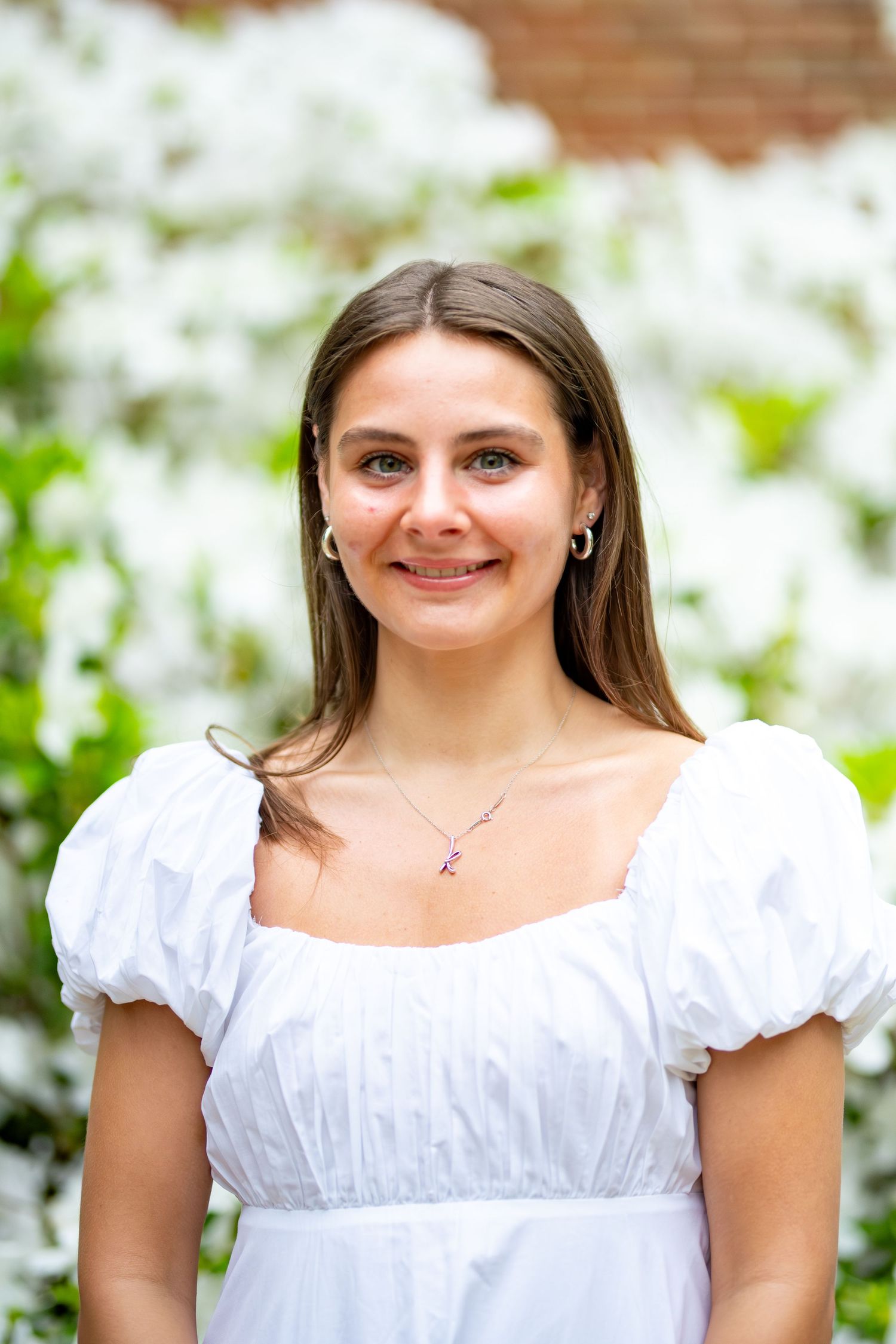 A person poses in a white puffy-sleeved dress against a floral spring background.