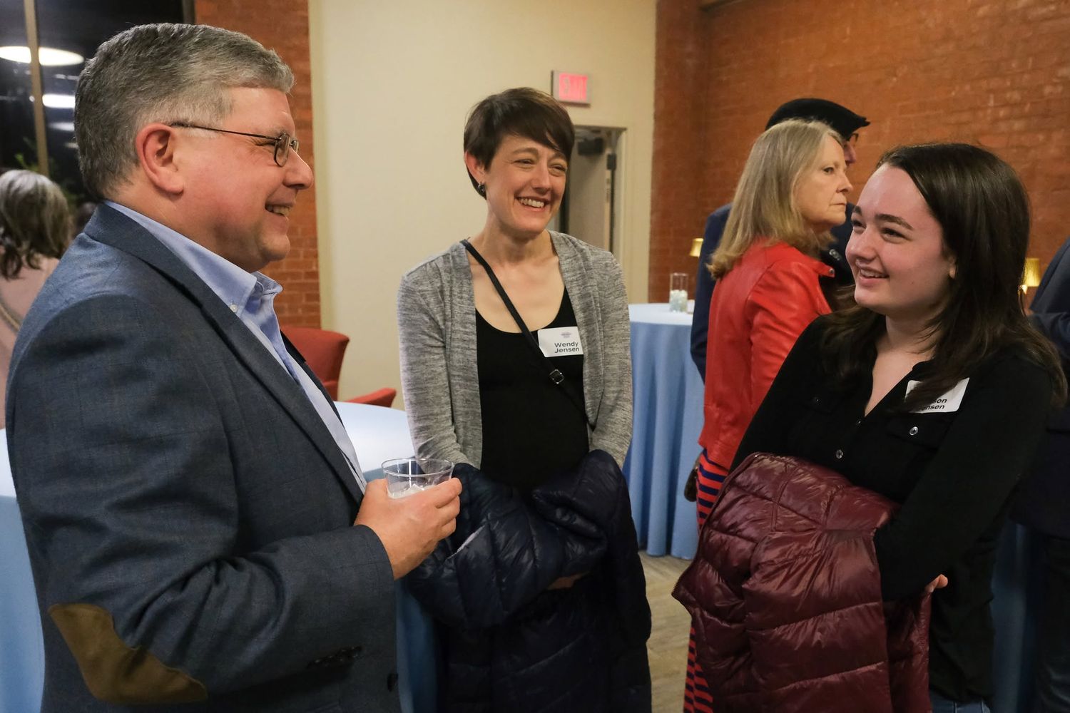 Three professionals networking and smiling during a business event in a brick-walled venue.
