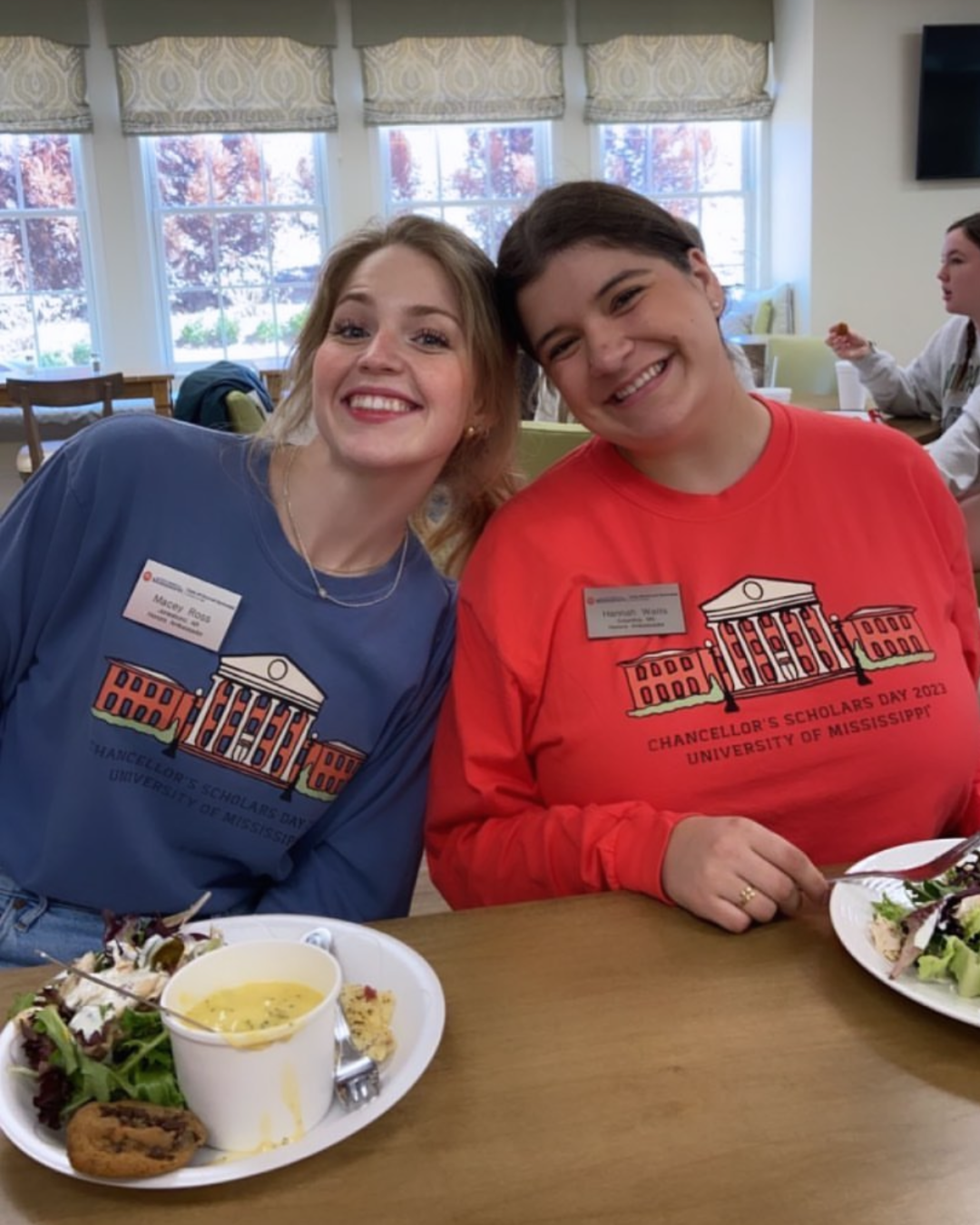 Two smiling women wearing University of Mississippi Chancellor's Scholars sweatshirts dining together at a table.