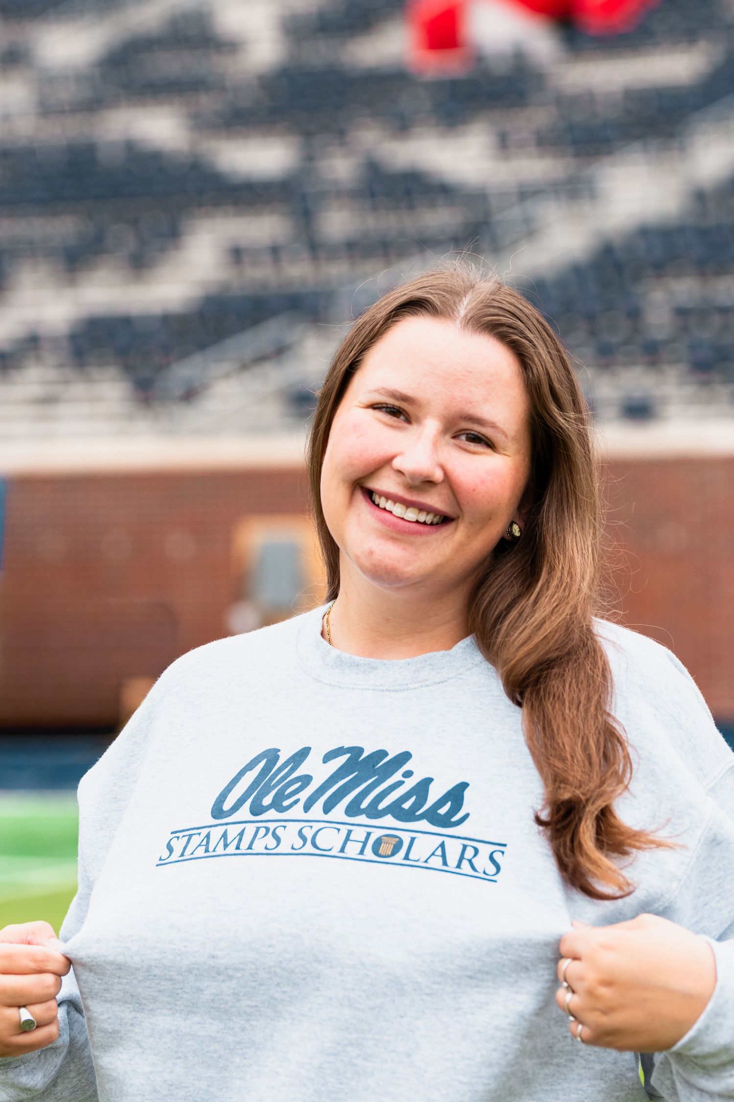 Smiling young woman wearing an Ole Miss Stamps Scholars gray sweatshirt standing in a football stadium.