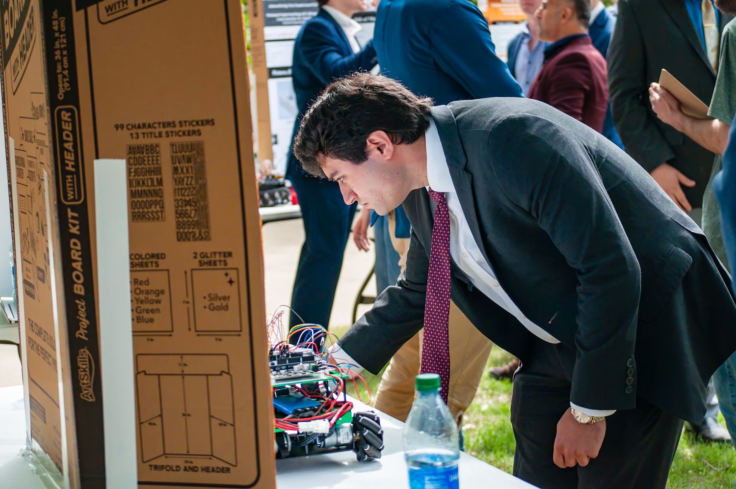 Young man in suit examining a robotics kit at a tech showcase event.