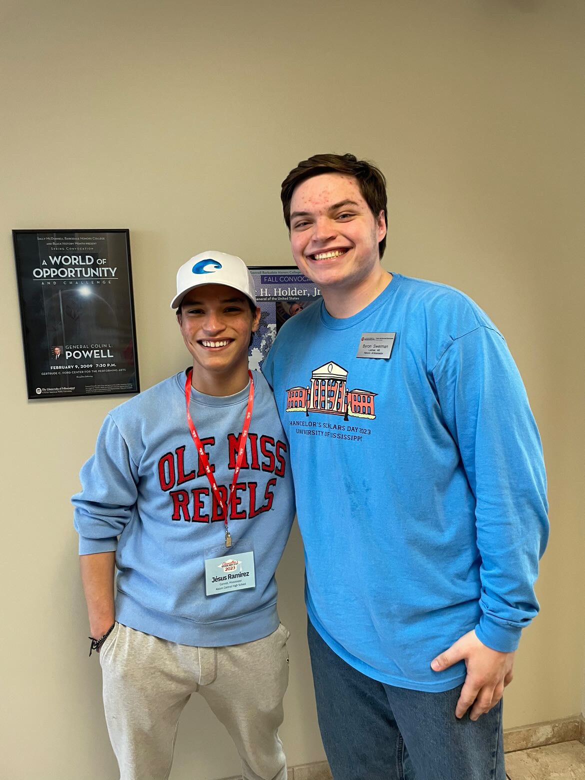 Two smiling young men wearing Ole Miss Rebels sweatshirts pose together indoors near a World of Opportunity poster.