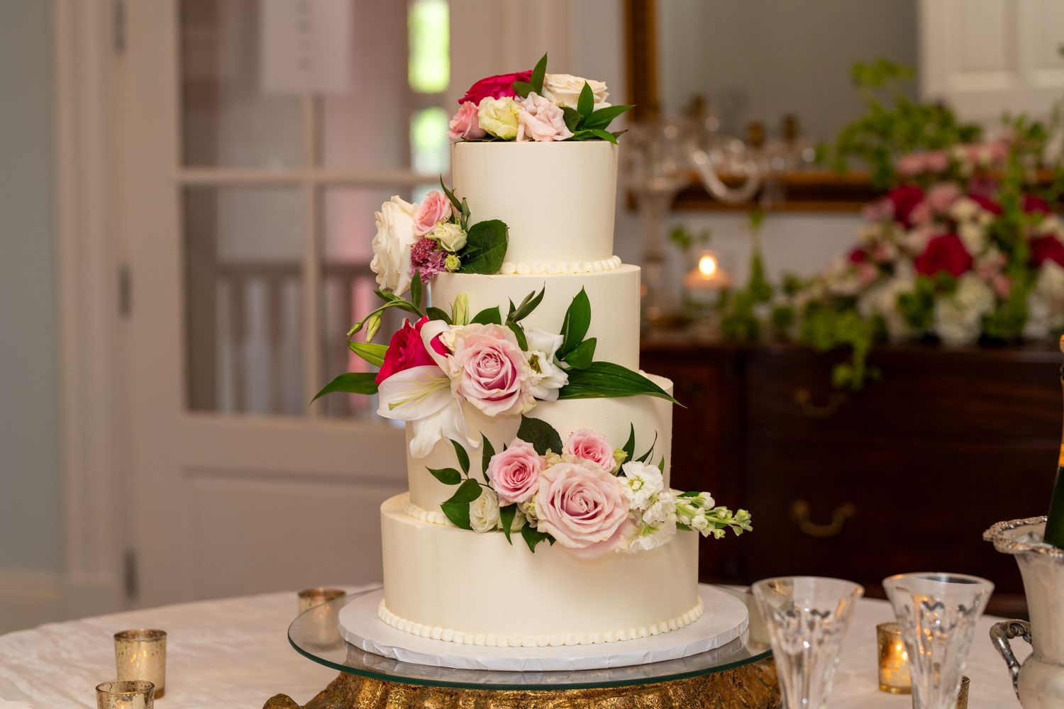Elegant white tiered wedding cake decorated with cascading pink roses and greenery on a gold stand.