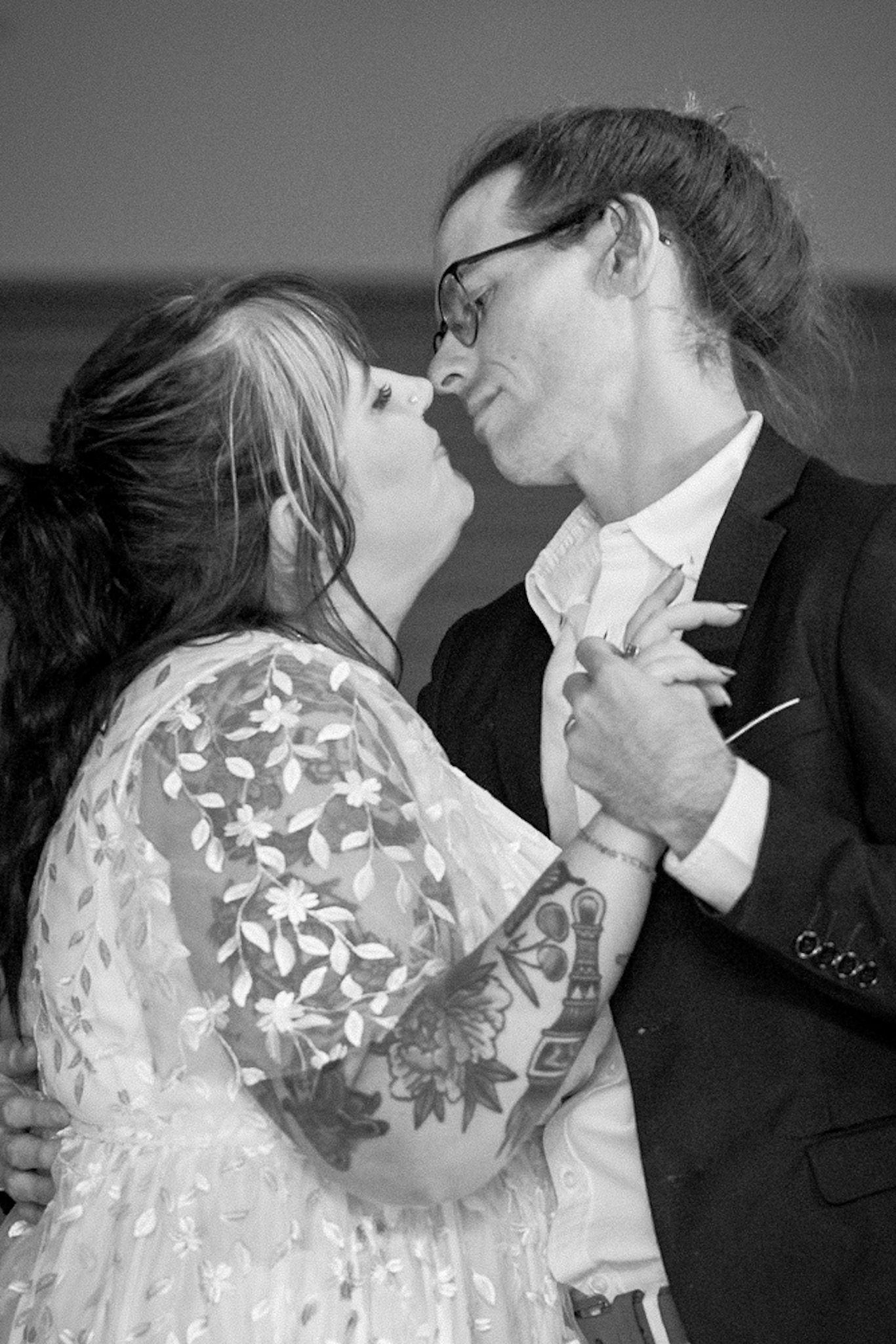 A romantic black and white photograph of a couple sharing an intimate kiss during their wedding dance.