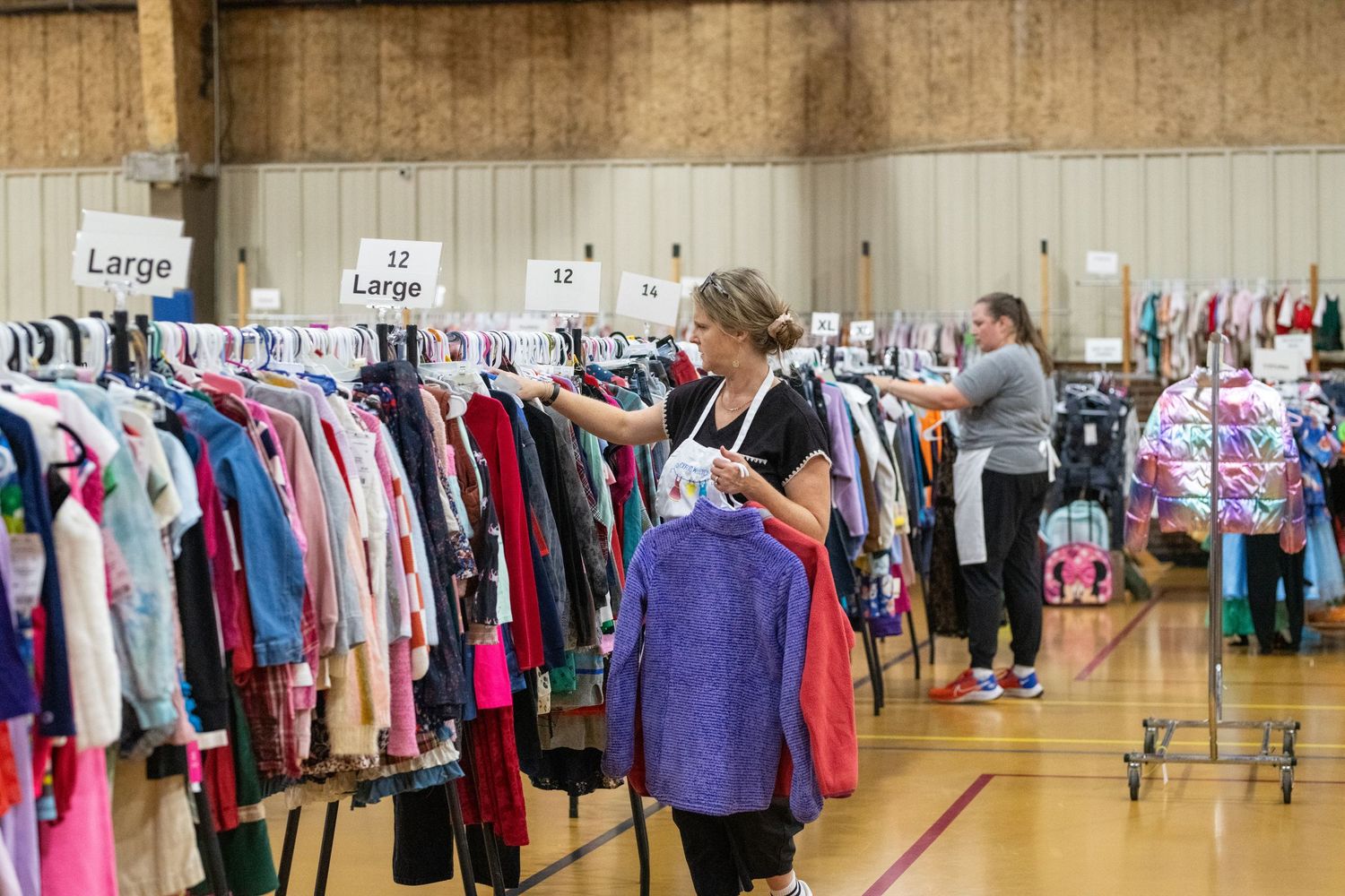 Women browsing organized clothing racks by size at an indoor consignment or thrift sale event.