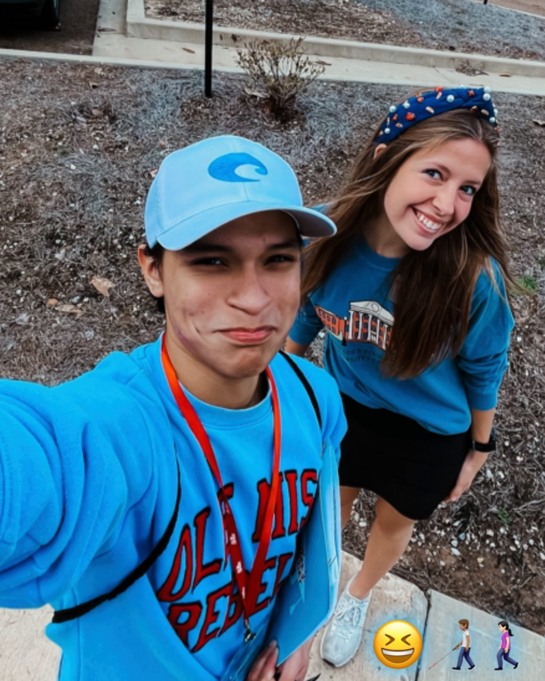 Two young people in matching blue Ole Miss sweatshirts smile for a selfie outdoors on a sunny day.
