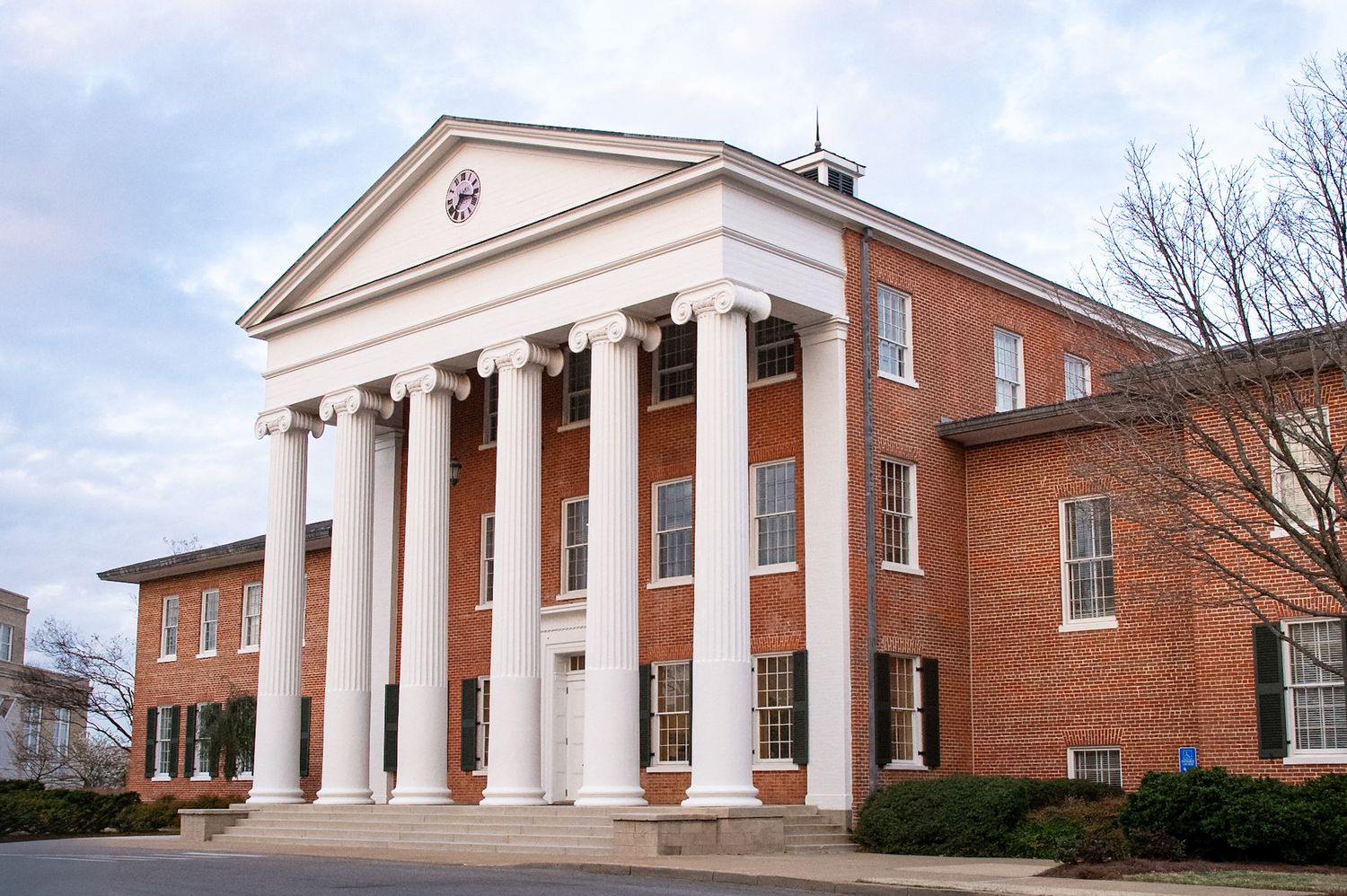 Historic brick university building with white Greek Revival columns and portico under a cloudy sky.