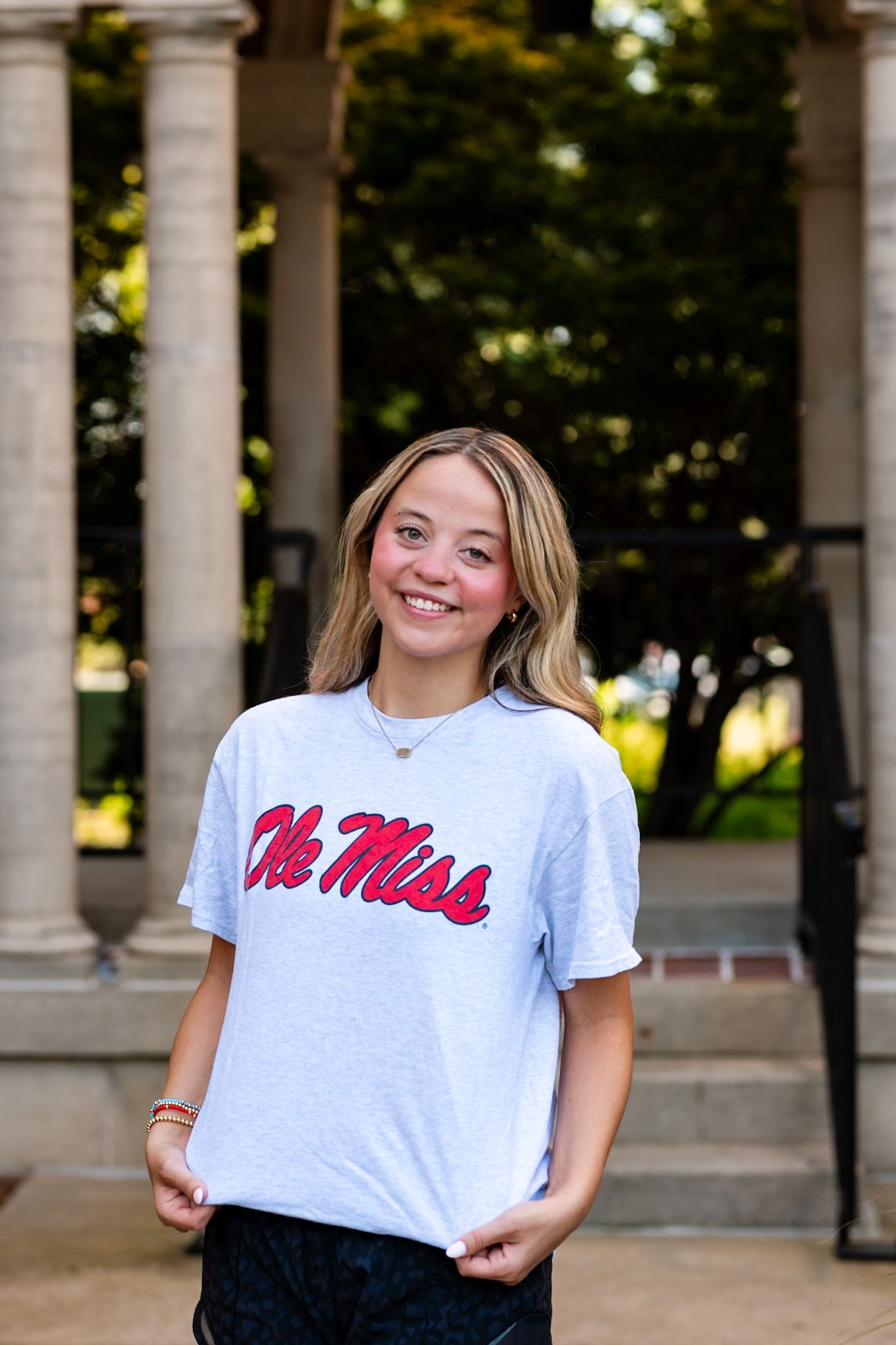 Smiling young woman wearing an Ole Miss t-shirt posing outdoors near columns.