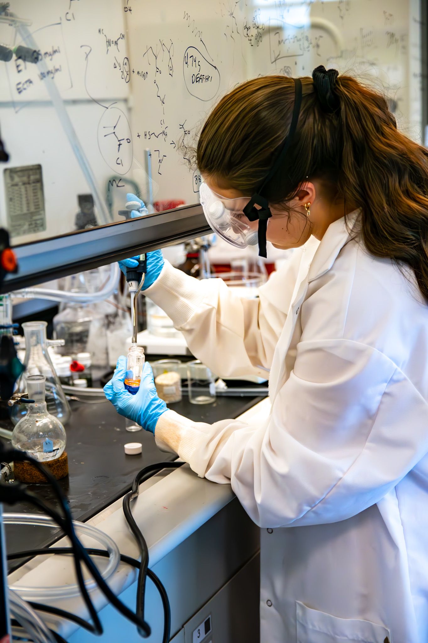 Female scientist in white lab coat and safety goggles conducting chemistry experiment in laboratory.