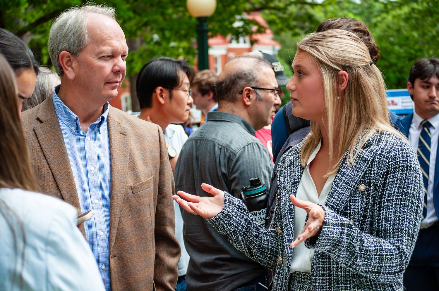 Two professionals engaged in conversation at an outdoor networking event with a crowd in the background.