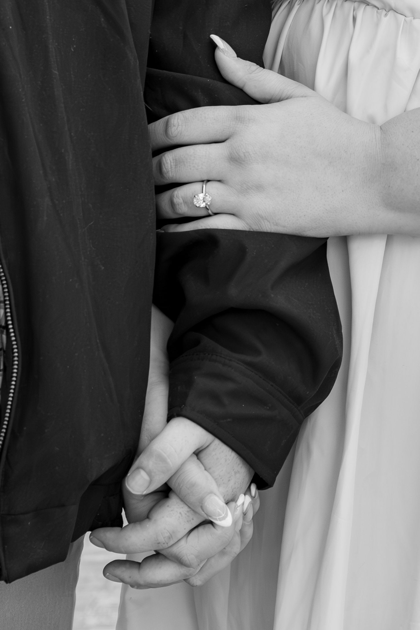 Close-up black and white photo of hands holding with engagement ring visible.
