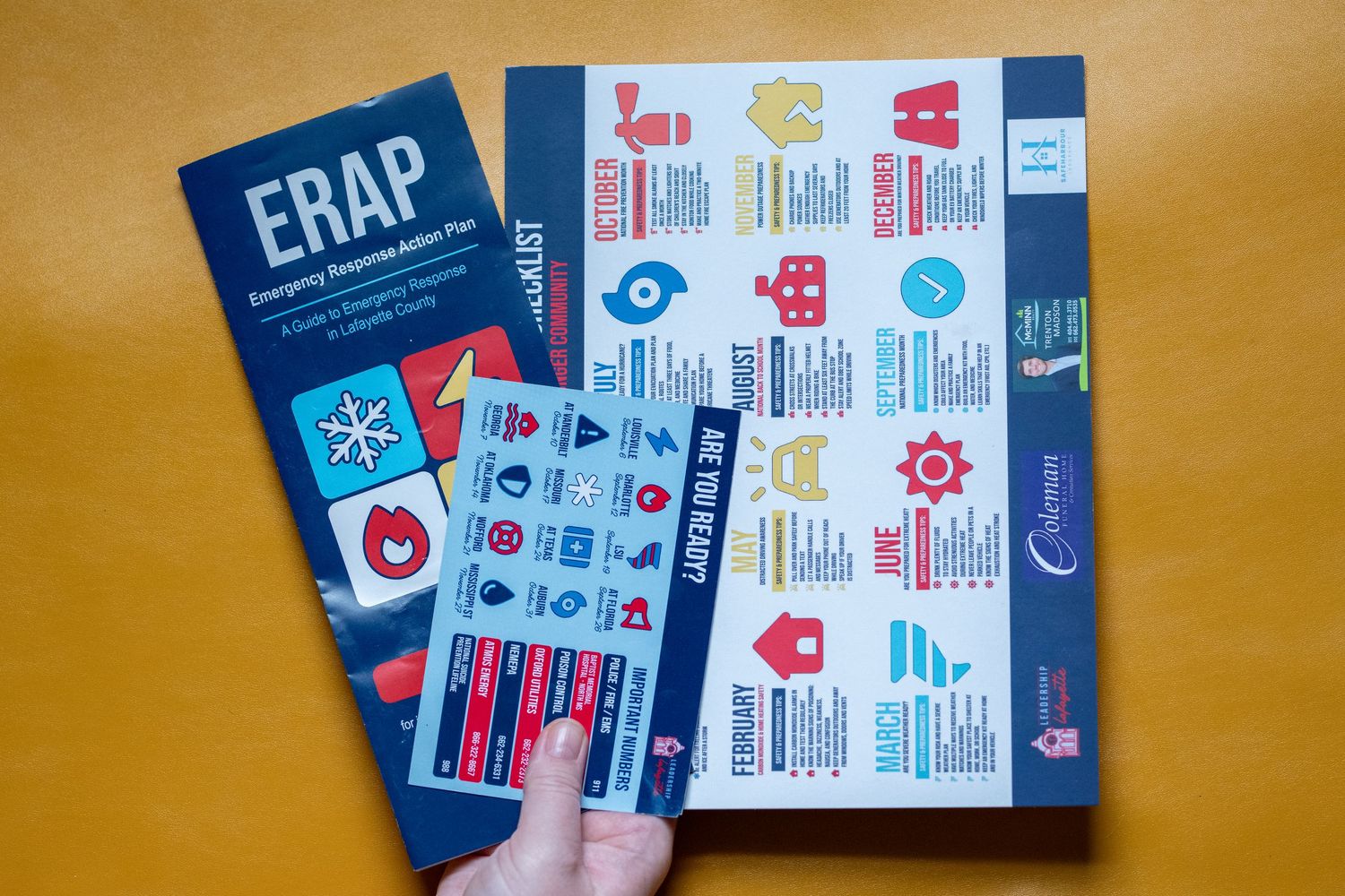 Hand holding ERAP Emergency Response Action Plan brochure next to a colorful checklist booklet on yellow background.