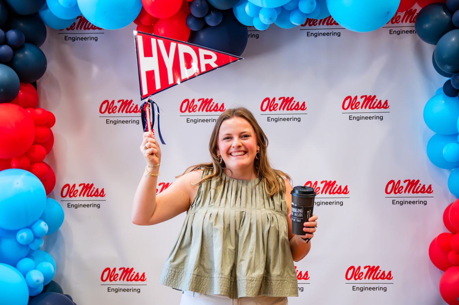 People pose against a red and blue balloon backdrop with Ole Miss branding at a photo opportunity event.