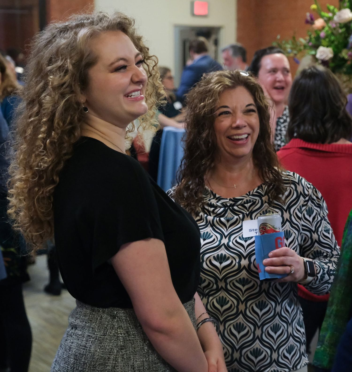 Two women smiling and laughing at a social gathering event.