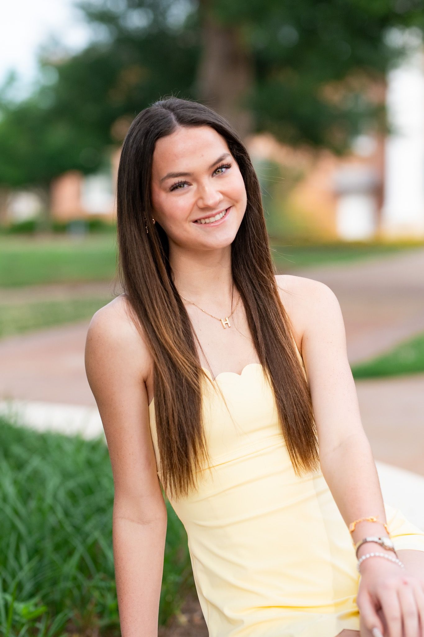 Smiling young woman in a yellow strapless dress posing outdoors on a sunny day.