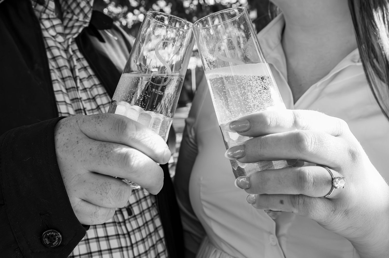 Close-up black and white photo of two people toasting with wine glasses.